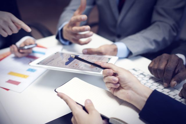 a group of people sitting around a table with a tablet.